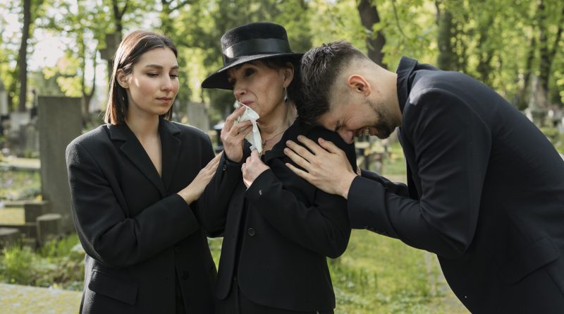 Bliscy w czarnych strojach żałobnych wspierający się i płaczący na cmentarzu podczas ceremonii pogrzebowej