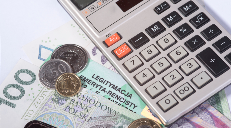 Polskie banknoty, monety oraz legitymacja emeryta-rencisty ZUS leżące obok kalkulatora biurowego.
