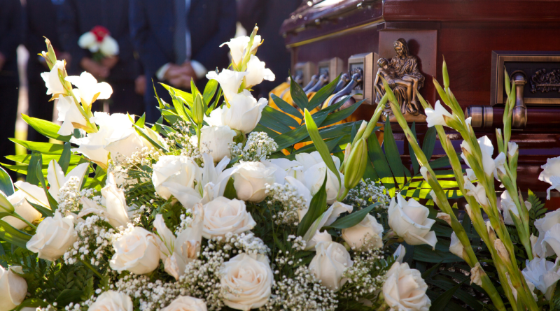 Elegancki wieńca pogrzebowy z białych róż i lilii ustawiony przed drewnianą trumną z mosiężnymi zdobieniami